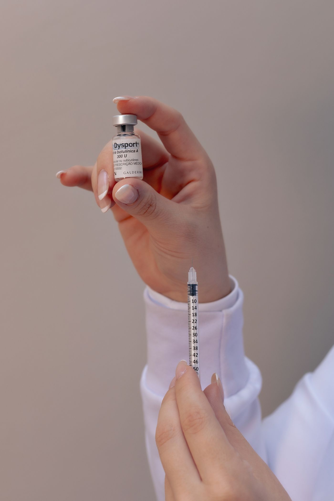 Manos con guante preparando una jeringa cosmetica y un vial